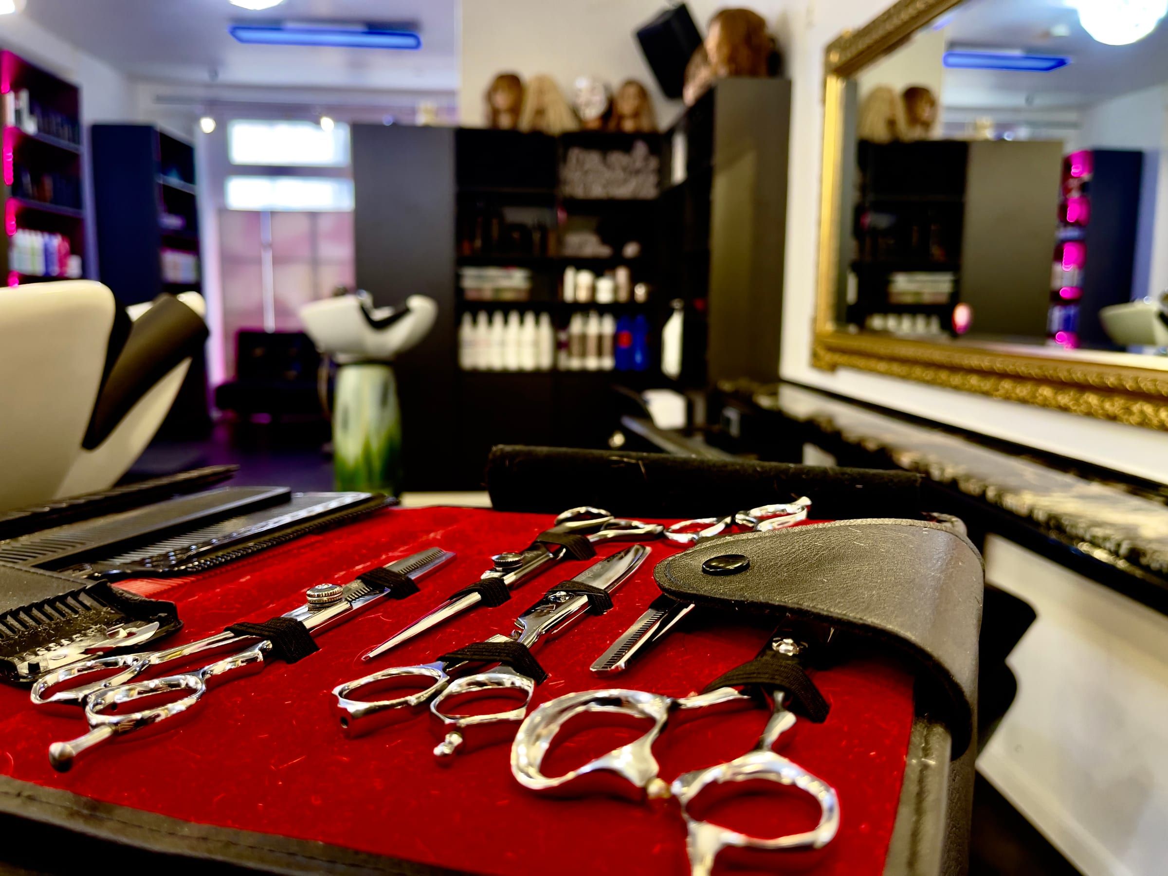 Blick in den Salon: Scheren auf rotem Tuch, dahinter Spiegel und Bedienplätze